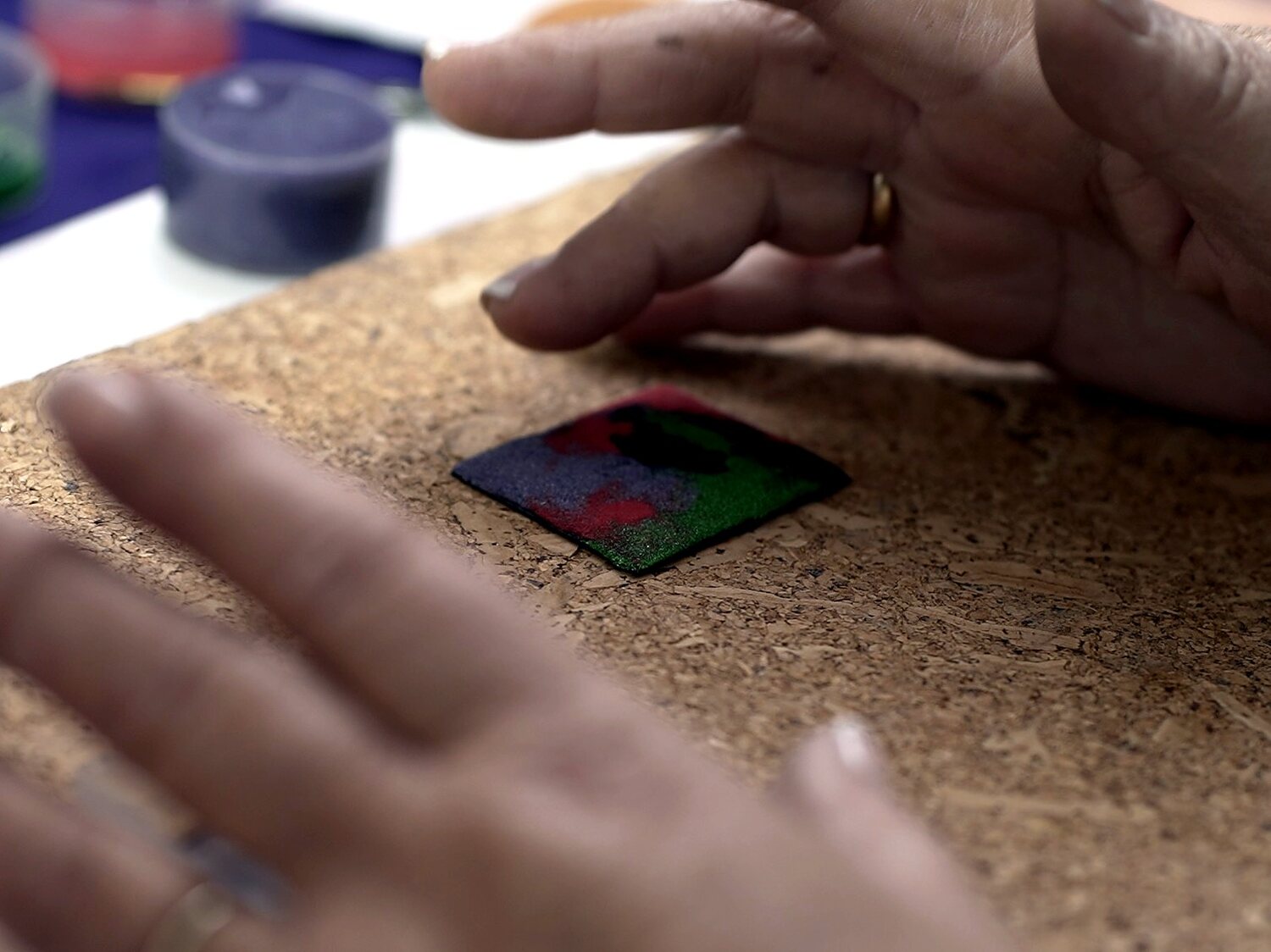 Manos colocando una placa de cobre esmaltada sobre el corcho de trabajo