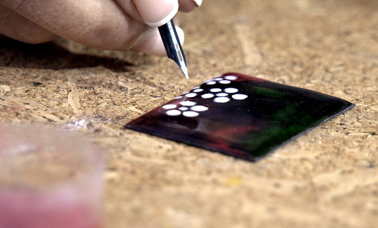 Pincel aplicando pequeñas flores blancas sobre esmalte oscuro